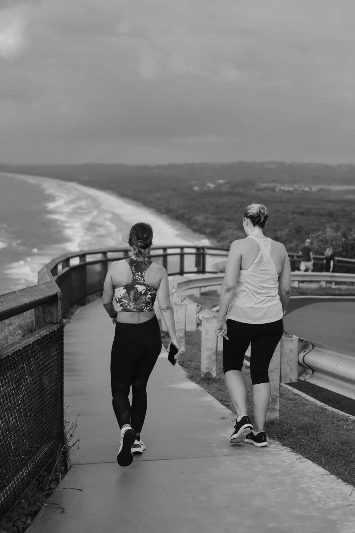 women walking to show how they make fitness progress walking together on a path which looks over the beach seen from behind