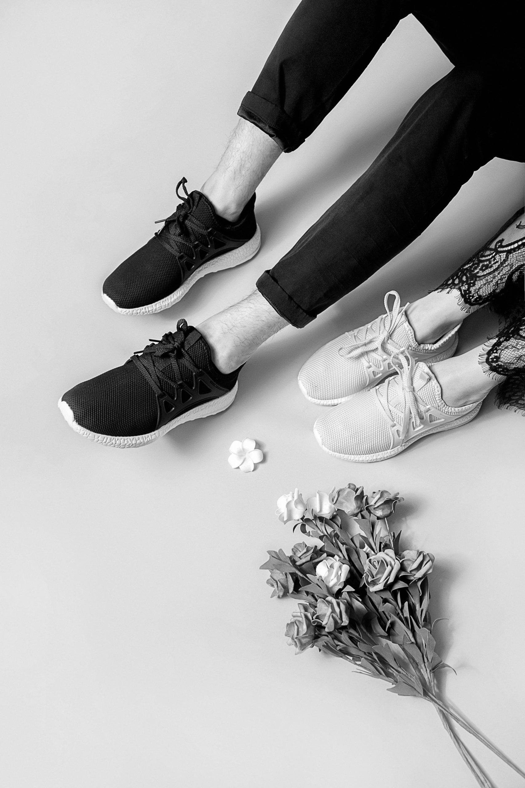 two people wearing shoes for crossfit and tights sitting next to a bouquet of flowers on a blank background