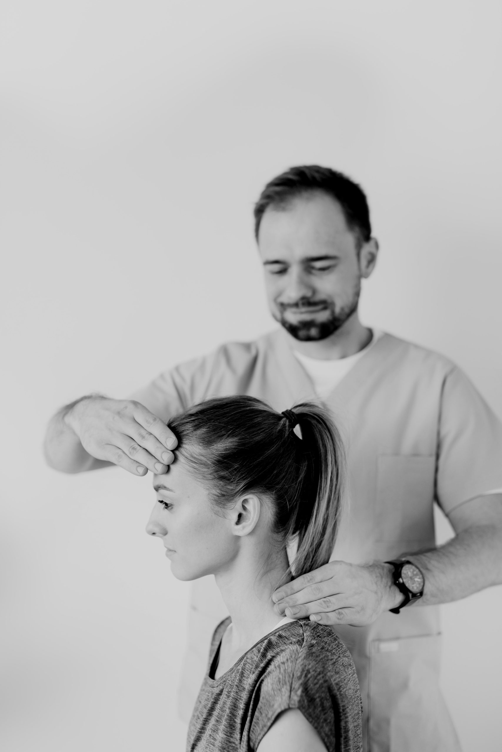massage therapist standing next to sitting woman touching her head and helping her start working out after an injury by giving her a massage
