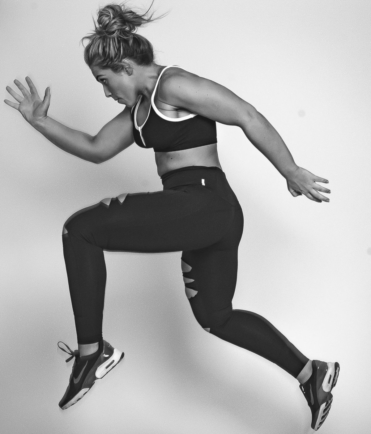 woman makes a good athlete wearing tights sneakers and sports bra in a running pose with hair in messy bun