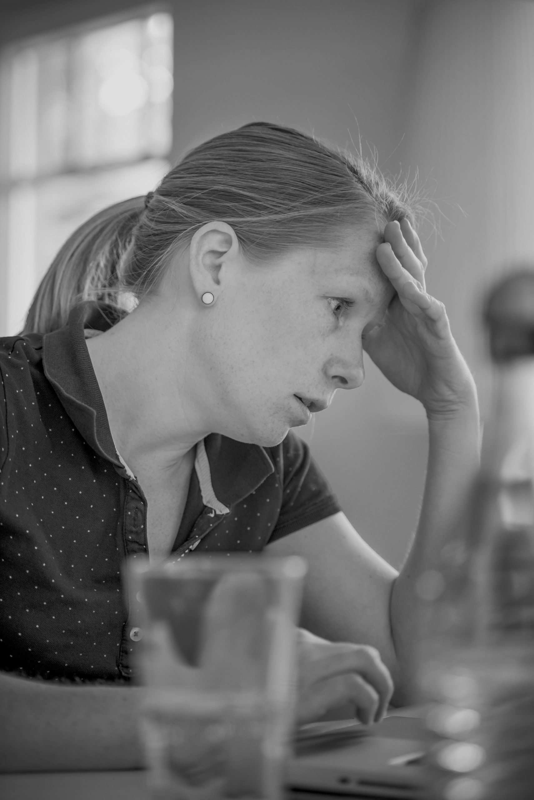 woman with stress affecting fitness with hair in ponytail and wearing a polo shirt sitting with her hand on her face at a table and with an expression of stress